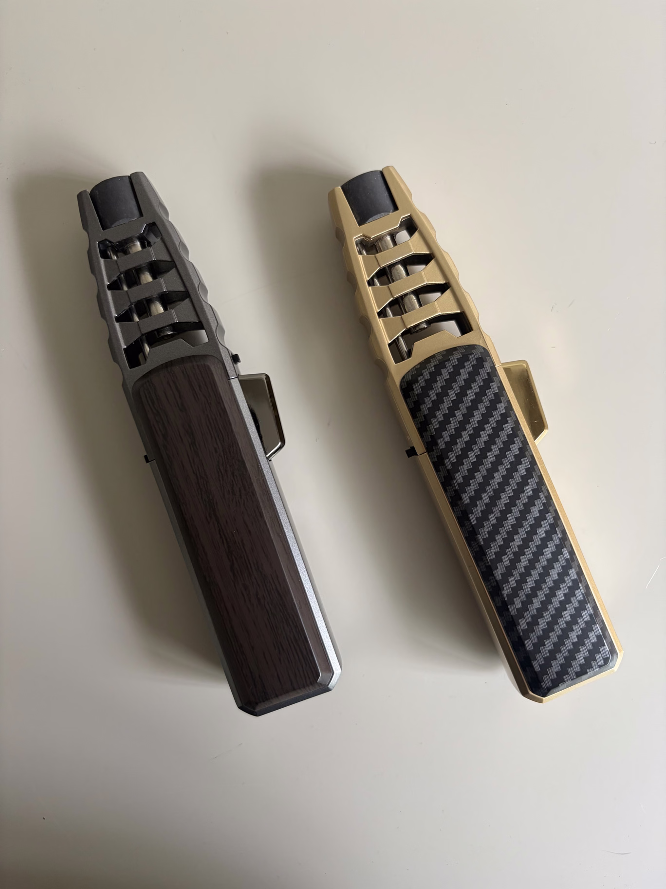 Zwei Feuerzeuge nebeneinander: ein dunkles Modell in Holzoptik und ein goldfarbenes Modell mit schwarzer Carbon-Optik